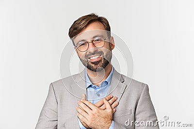 Close-up of handsome businessman in gray suit and glasses, holding hands on heart and thanking for something, smiling Stock Photo