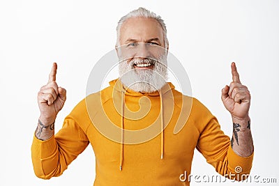 Close up of handsome hipster senior pointing fingers up and smiling happy. Old man with beard and tattoos showing Stock Photo