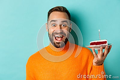 Close-up of happy adult man celebrating birthday, holding bday cake with candle and making wish, standing against Stock Photo