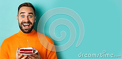 Close-up of happy adult man celebrating birthday, holding bday cake with candle and making wish, standing against Stock Photo