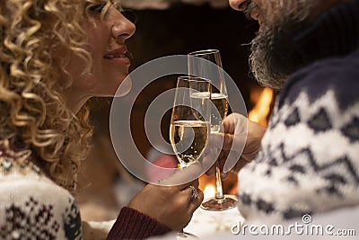 Close up of happy couple in love clinking flutes of wine with fired fireplace in background. Romantic people enjoying relationship Stock Photo