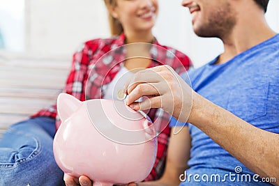 Close up of happy couple putting coin to piggybank Stock Photo