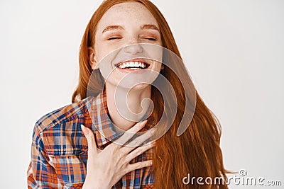 Close-up of happy smiling woman with red natural hair and pale skin, holding hand on heart and laughing with eyes closed Stock Photo