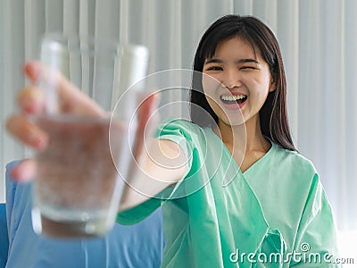 Close up of happy young inpatient woman who is getting well from her ailment smiling on to camera and holding a glass of water in Stock Photo