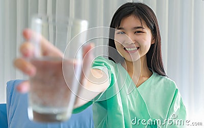 Close up of happy young inpatient woman who is getting well from her ailment smiling on to camera and holding a glass of water in Stock Photo