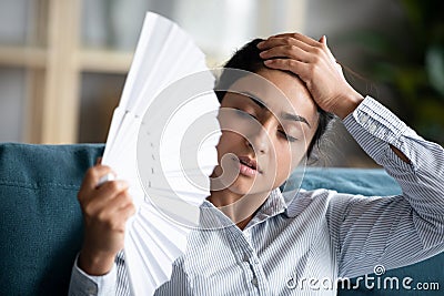 Overheated young indian woman cooling herself with paper fan. Stock Photo