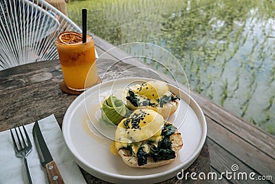 Close up Healthy Breakfast with Bread Toast and Poached Egg with spinach, avocado on wooden table with view on rice field. Orange Stock Photo