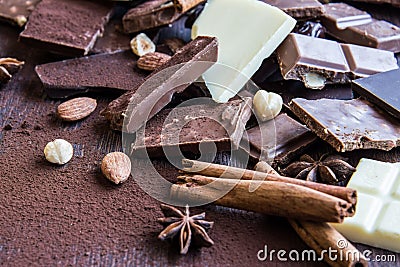 Close up of a heap of various chocolate pieces over dark wood background. Dark, milk, white and nuts chocolate bars. Cinnamon, sta Stock Photo