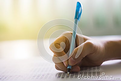 Close up of high school or university student holding a pen writing on answer sheet paper in examination room. College students an Stock Photo