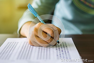 Close up of high school or university student holding a pen writing on answer sheet paper in examination room. College students an Stock Photo