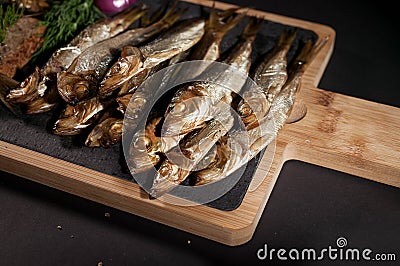 Close-Up Hot smoked sprat, red onion and dill on a cutting board on a dark background Stock Photo