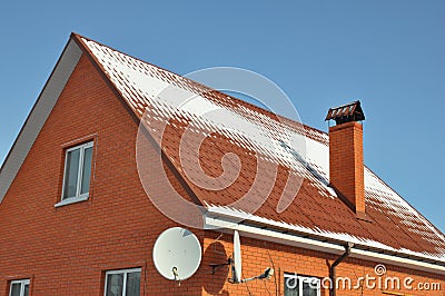 A close-up of a house from red brick with two satellite dish antennas, rain gutter system, a chimney, and a gable steep metal Stock Photo