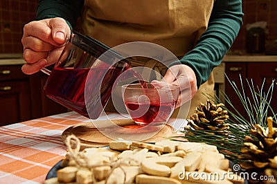 Close-up housewife pouring hibiscus tea from a teapot into a glass cup, standing by a table with gingerbread cookies Stock Photo