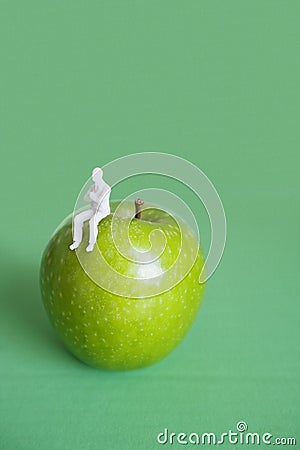 Close-up of human figurine sitting on green apple over colored background Stock Photo