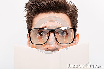Close-up image of Confused nerd in eyeglasses hiding behind book Stock Photo