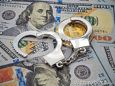 Close-up image of a pair of handcuffs on a Bitcoin coin over a pile of dollar bills Stock Photo