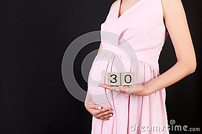 Close up image of thirty weeks of pregnancy cubes in pregnant woman`s hands at black background. Happy pregnancy. Copy space Stock Photo