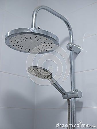 Close-up image of two shower heads in white tile bathroom. large is mounted on metal pipe and small attached to flexible hose Stock Photo