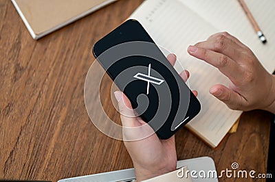 Close-up image of a woman using X Twitter platform on her Iphone14 at her desk Editorial Stock Photo