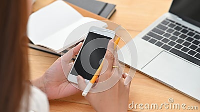 Close-up image of young creative woman while holding/using a black blank smartphone on the working desk. Stock Photo