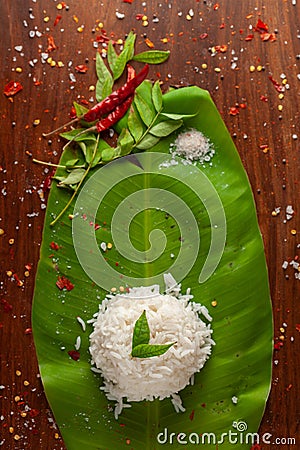 Close-up of Indian cooked rice over the banana fresh green leaf. Garnished with curry-patta leaves and red chilli paper Stock Photo