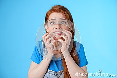 Close-up intense panicking redhead woman watching scary movie feel pressured, biting lip worried, hold hands near mouth Stock Photo