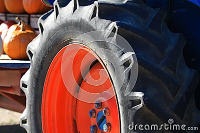 Close up of isolated black wheel tire with deep sufficient tread of antique old tractor with red rim and blue nuts on a farm in Stock Photo