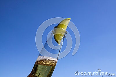Close up of isolated bottleneck with sparkling yellow beer and a slice of lime against cloudless deep blue sky Stock Photo