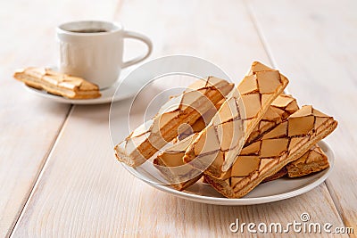 Close-up of Italian crispy bakery Sfogliatine glassate on a white saucer and cup of hot coffee over white wooden table. Sweet Stock Photo
