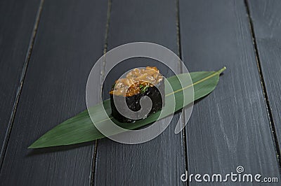 Close up of Japanese Gunkan Sake Maki Sushi roll with marinated salmon and greens on bamboo leaf on black wooden board. Stock Photo