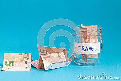 close up of a jar with travel label filled with paper money euro and other money on the side, blue background Stock Photo