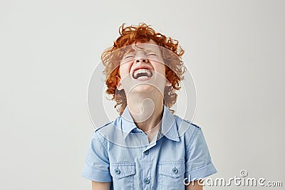 Close up of joyful little kid with ginger curly hair and freckles in blue shirt laughing hard watching comedy with Stock Photo