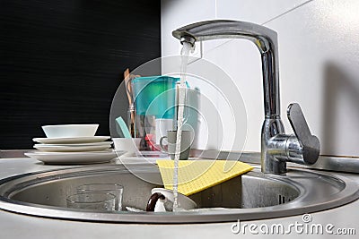 Close-up of a kitchen sink with dirty dishes in a home interior. Water flows from an open tap Stock Photo