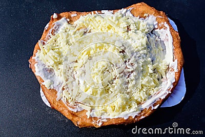 Close up of a langos, typical Hungarian food specialty, with sour cream and cheese on a white dish on a dark grey table, deep frie Stock Photo