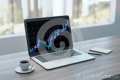 Close up of laptop on desktop with coffee cup, notepad and glowing candlestick forex chart hologram on blurry background. Trade Stock Photo