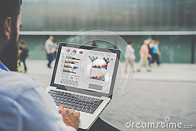 Close-up laptop with graphs, diagrams and charts on screen in hands of businessman sitting outdoors and working. Stock Photo