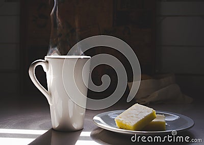 Close up of large coffee mug with steam and lemon cake on a plate Stock Photo