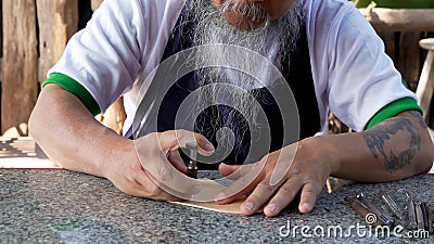 Close-up of leather worker's hand, seen with long beard, cutting cowhide printed on cowhide for cutting and trimming. Stock Photo