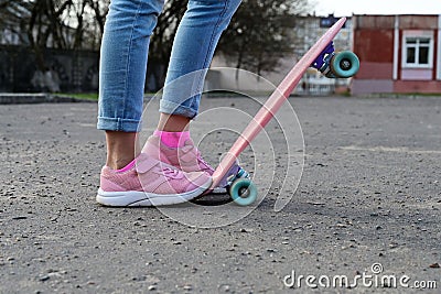 Close-up legs of girl skateboarder in blue jeans and pink sneakers, riding pink penny skate longboard. Stock Photo