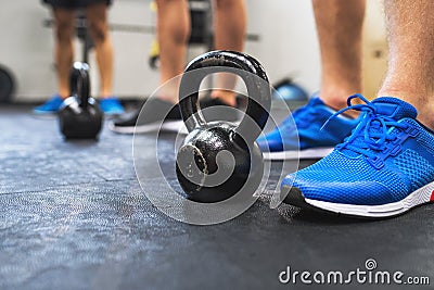 A close-up of legs of three men in gym standing by kettlebells. Stock Photo