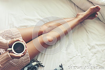 Close up legs women on white bed. Women reading book and drinking coffee in morning relax mood in winter season. Stock Photo