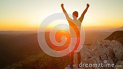 LENS FLARE: Male tourist celebrates reaching top of the mountain at sunrise. Stock Photo