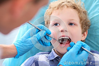 Close-up of little Caucasian curly boy opening his mouth wide during inspection of oral cavity by dentist. Stock Photo