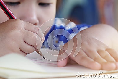 Close-up little girl childâ€™s hand holding pencil drawing on notebook white paper, homeschool education concepts Stock Photo