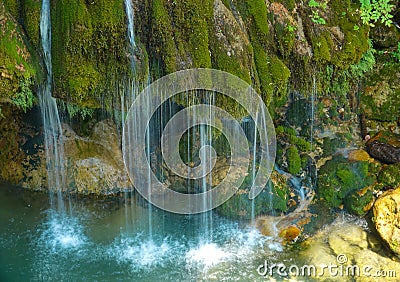 CLOSE UP: Little streams running down the green rocks and into the emerald lake. Stock Photo