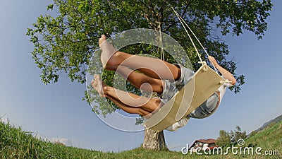 CLOSE UP LOW ANGLE: Unrecognizable young woman and man swaying on wooden swing. Stock Photo