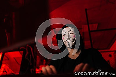 Close-up low-angle view of dangerous hacker man wearing anonymous mask and sweatshirt typing code on keyboard late night Editorial Stock Photo