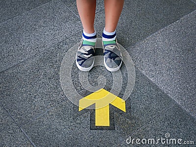 Low Section of Kid Standing In Front Of Yellow Directional Arrow Stock Photo