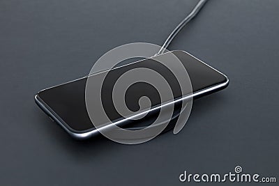 Close-up of luxury smartphone while recharging battery using wireless charger. Matt grey desk surface in background Stock Photo