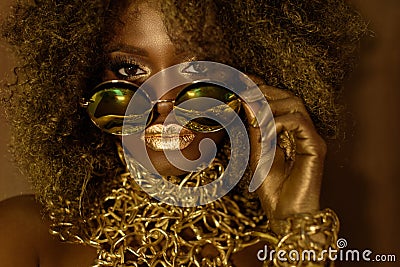 Close-up of magic golden african american female model in massive sunglasses with bright glitter makeup, glossy Stock Photo